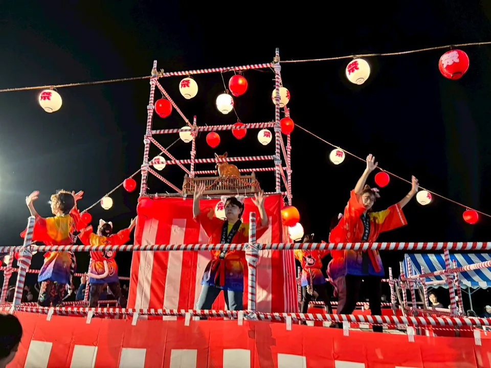 会場中央に設置された櫓と頂上の白ニャン菩薩像。提灯の灯りに照らされたダンスの様子